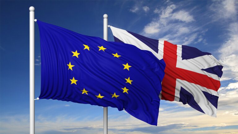 Waving flags of EU and UK on flagpole, on blue sky background